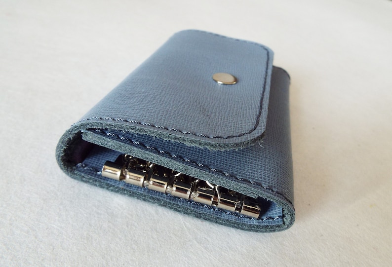 May include: A blue leather key holder with a metal key ring. The key holder has a flap that closes with a snap.