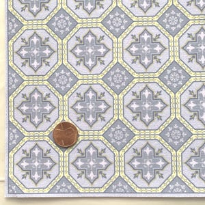 May include: A sheet of gray and yellow patterned paper with a repeating geometric design. The paper is textured and has a subtle sheen. A US penny is placed on the paper for scale.