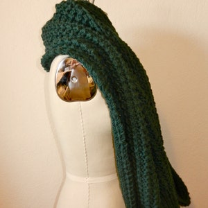 May include: A dark green knitted scarf draped over a white dress form.