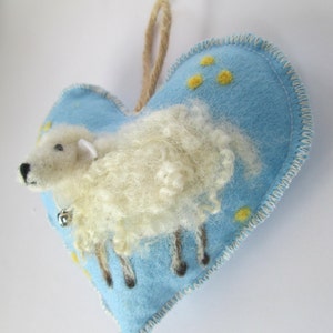 May include: A blue felt heart-shaped ornament with a white fluffy sheep and yellow dots. The sheep has a bell on its collar.