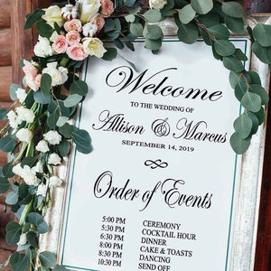May include: A wedding welcome sign on a wooden easel. The sign has a silver frame and features the words "Welcome" and "Order of Events." The sign is decorated with flowers and greenery. The wedding date is September 14, 2019.