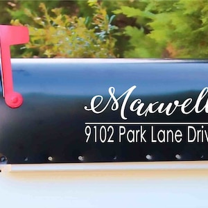 May include: Black mailbox with the name "Maxwell" in white script and the address "9102 Park Lane Drive" in a clean font. The mailbox has a red flag and is set against a backdrop of green foliage.