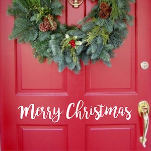 以下が含まれることがあります： 赤いドアにクリスマスのリースと白い筆記体で「Merry Christmas」の文字。リースは常緑樹の枝、松ぼっくり、赤い実でできています。金色のドアノブとノッカーが見えます。