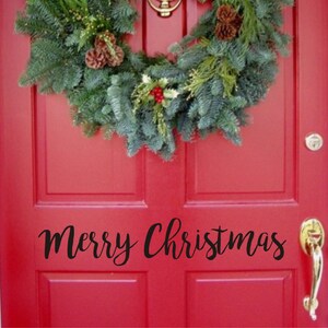 以下が含まれることがあります： 赤いドアにクリスマスのリースと黒い筆記体で「Merry Christmas」の文字。 リースは常緑樹の枝、松ぼっくり、赤い実でできています。 金色のドアノブとノッカーが見えます。