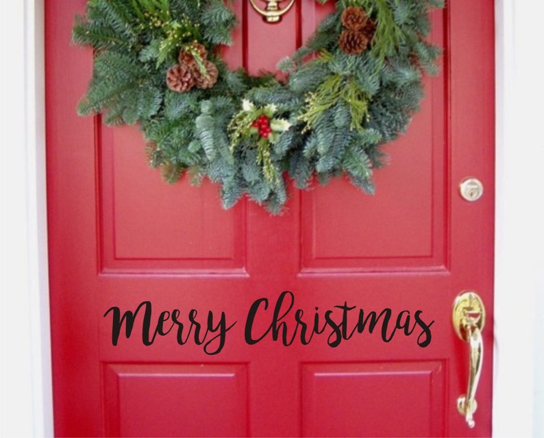 以下が含まれることがあります： 赤いドアにクリスマスのリースと黒い筆記体で「Merry Christmas」の文字。 リースは常緑樹の枝、松ぼっくり、赤い実でできています。 金色のドアノブとノッカーが見えます。