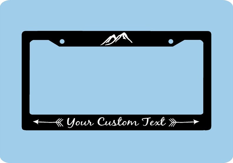 Pode incluir: Moldura preta para placa de carro com um gr&aacute;fico de montanhas brancas no topo. O texto "Your Custom Text" est&aacute; em branco, emoldurado por setas. A moldura tem formato retangular.