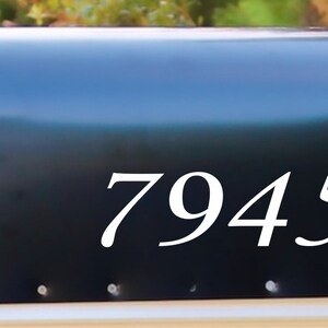 May include: A black mailbox with the white numbers 79452 displayed prominently on the side. The mailbox has a red flag and is set against a blurred green background.