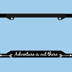May include: Black license plate frame with the text "Adventure is out there" in white script. The frame has a rectangular shape with rounded corners and a light blue background.