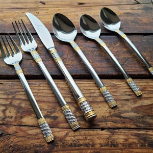 Puede incluir: Un juego de seis piezas de cubiertos de plata y oro, incluyendo tenedores y cucharas, con intrincados patrones en los mangos.