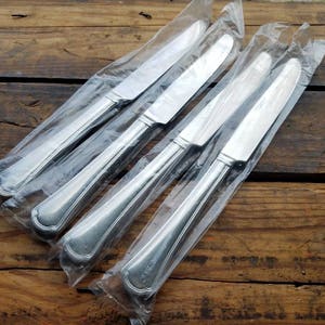 May include: Four silver dinner knives wrapped in clear plastic packaging.