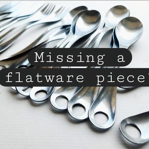 Puede incluir: Un conjunto de cubiertos plateados brillantes, que incluyen cucharas y tenedores, dispuestos sobre una superficie blanca. El texto "Missing a flatware piece?" está presente.
