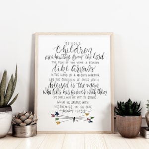 May include: A framed print with calligraphy text, including the words "Children are a heritage from the Lord." The print is in a light wood frame and is displayed with potted plants. The text also includes the bible verse Psalm 127:3-5.