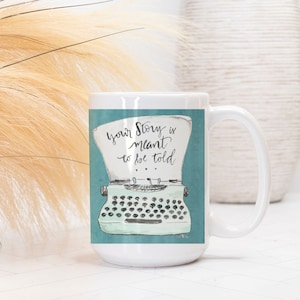 May include: White ceramic mug with a teal blue background and a vintage typewriter illustration. The text on the mug reads "Your story is meant to be told."