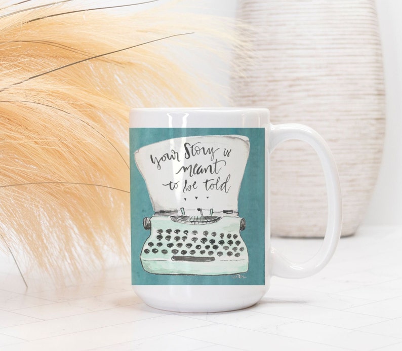 May include: White ceramic mug with a teal blue background and a vintage typewriter illustration. The text on the mug reads "Your story is meant to be told."