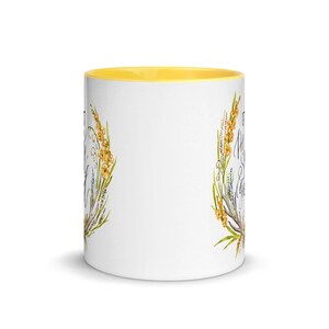 May include: White ceramic mug with a yellow interior. The mug features a floral design with yellow and green accents, and script text. The mug is a standard size for coffee or tea.