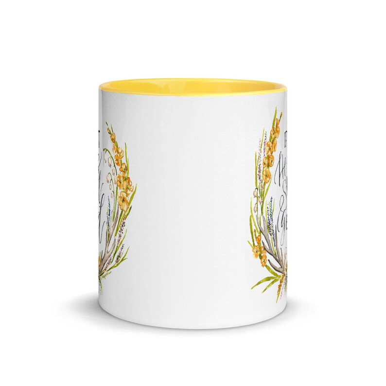 May include: White ceramic mug with a yellow interior. The mug features a floral design with yellow and green accents, and script text. The mug is a standard size for coffee or tea.