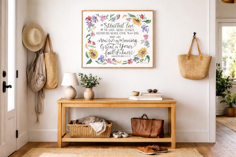 Puede incluir: Una impresi&oacute;n floral enmarcada con el texto "El amor constante del Se&ntilde;or nunca cesa". Una consola de madera exhibe una l&aacute;mpara, un jarr&oacute;n, libros y una bolsa de cuero. Una bolsa de paja y un sombrero cuelgan de la pared.