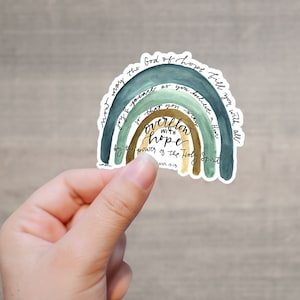 以下が含まれることがあります： 虹の形をしたステッカーに「希望の 神 は、あなたが 信じる ことによって、喜びと平安であなたを満たし、聖霊の 力 によって、あなたは希望にあふれるでしょう。」ローマ人への手紙 15:13 と書かれています
