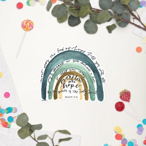 以下が含まれることがあります： 水彩の虹とローマ人への手紙 15:13 の引用文「希望の 神 が、あなたがたを信仰におけるすべての喜びと平安で満たし、聖霊の力によって、あなたがたが希望にあふれるようにされますように。」