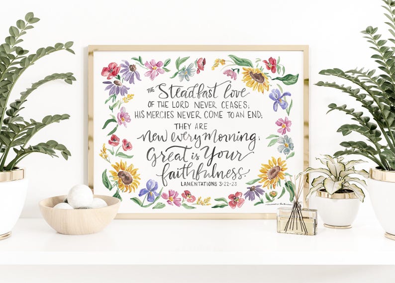 Puede incluir: Una impresi&oacute;n en acuarela enmarcada con el texto "El amor constante del Se&ntilde;or nunca cesa...Grande es tu fidelidad". La obra de arte est&aacute; rodeada por una corona floral de girasoles, margaritas y otras flores coloridas. El marco es de color madera clara.