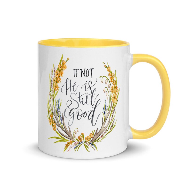May include: White ceramic mug with a yellow interior and handle. The mug features the text "IF NOT He is Still good" in a handwritten style, surrounded by a floral wreath with yellow and green accents.