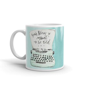 May include: White ceramic mug with a light blue background featuring a vintage typewriter with the text "Your Story is meant to be told".
