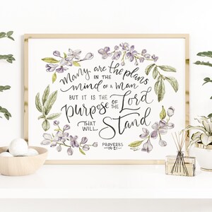 Könnte beinhalten: Ein gerahmter Aquarelldruck mit dem Zitat "Viele Pläne sind im Herzen des Menschen, aber der Ratschluss des Herrn wird bestehen." Das Kunstwerk zeigt florale und Blattakzente in Lila und Grün.