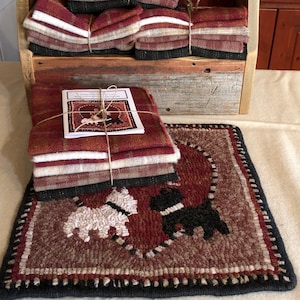 May include: A set of wool fabric squares in red, white, and black plaid patterns, bundled together with twine. The fabric squares are in a wooden crate. A rug with a heart design and two dogs is in the foreground. The rug is made with wool yarn in shades of red, brown, black, and white.