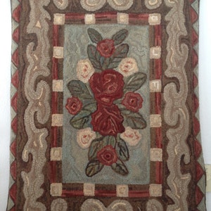 May include: Rectangular, hand-stitched pillow with a floral design. The central motif features a cluster of red roses and white roses with green leaves on a light blue background. The border is brown with decorative scrollwork and a red trim.