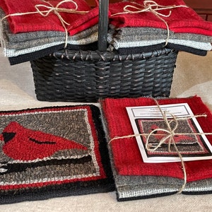 May include: A set of wool rug hooking kits featuring a cardinal bird design. The kits include wool yarn in red, gray, and black colors, and a pattern guide. The kits are packaged in a woven basket.