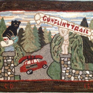 May include: A hooked rug depicting a red car driving on a road through a forest with a sign that reads "Gunflint Trail". A black bear is sitting on a rock in the background.