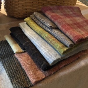 May include: A stack of various wool fabric swatches in shades of gray, brown, green, and red. The fabrics have different textures and patterns, including herringbone and plaid. The swatches are arranged in a fan shape.