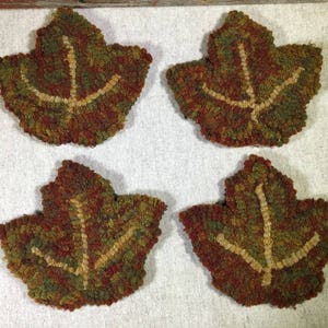 May include: Four handmade felt leaf-shaped coasters in shades of green, brown, and tan. The leaves have a raised design in a lighter tan color.
