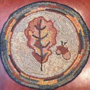 May include: A round, hand-woven rug with a brown and orange leaf design in the center. The rug has a blue and orange border.
