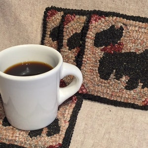 May include: Three square black and tan woven coasters with a black silhouette of a dog on each. A white mug with coffee is sitting on one of the coasters.