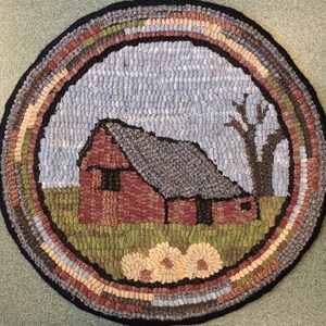 May include: A round, hand-hooked rug featuring a rural scene. The rug depicts a red barn with a gray roof, a leafless tree, and a field of flowers. The border has a black edge and a multi-colored design. The rug measures approximately 24 inches in diameter.