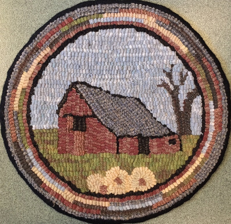 May include: A round, hand-hooked rug featuring a rural scene. The rug depicts a red barn with a gray roof, a leafless tree, and a field of flowers. The border has a black edge and a multi-colored design. The rug measures approximately 24 inches in diameter.
