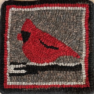 May include: A red cardinal perched on a black branch, surrounded by a gray and white border. The bird is depicted in a stylized, folk art style, with a simple, rounded shape and a black eye.