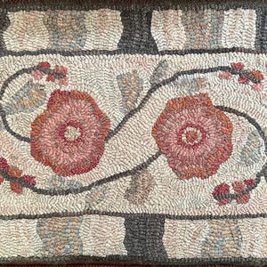May include: A rectangular hooked rug featuring a central cream-colored field with two large, textured floral motifs in shades of pink and red. The design includes winding stems and leaves, surrounded by a wide border of alternating dark gray blocks.
