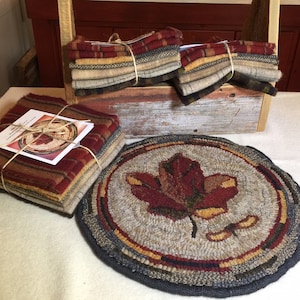 May include: A set of wool fabric squares in various shades of brown, red, and beige, bundled together with twine. The fabric squares are arranged in a wooden crate. A rug with a brown, red, and beige leaf design is in the foreground.