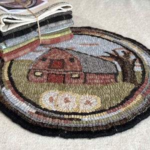 May include: A round, hand-hooked rug featuring a red barn scene with a gray roof, a tree, and a light blue sky. The rug has a black border and a stack of fabric squares tied with twine.