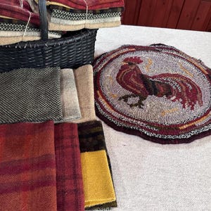 May include: A collection of wool fabric squares in various colors and patterns, including red, brown, yellow, and gray. The fabric squares are arranged in a pile on a white surface. A woven rug with a rooster design is also visible in the image.