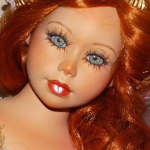 May include: A porcelain doll with long, flowing red hair and blue eyes. The doll is wearing a green and gold dress and has a delicate, feminine appearance.