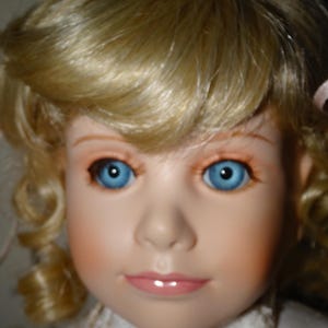 May include: A porcelain doll with blonde hair, blue eyes, and a white lace dress. The doll has a sweet and innocent expression.