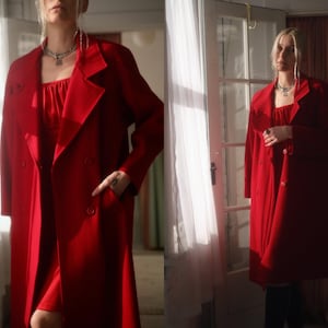 May include: A striking red coat with a double-breasted design and a matching red dress. The coat has a classic lapel and button closure. A silver necklace completes the look. The ensemble exudes elegance and confidence.