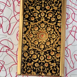May include: A gold-trimmed rectangular box with a black and gold patterned design. The pattern features intricate floral motifs and small, colorful jewels.