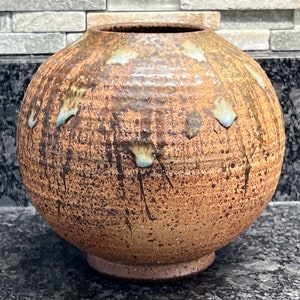 May include: A round, brown ceramic vase with a textured surface and blue glaze accents. The vase has a wide base and a narrow opening.