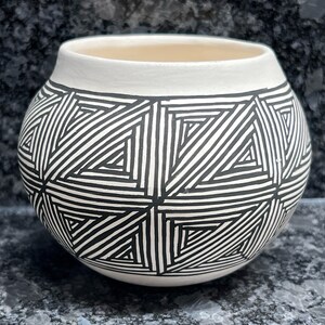 May include: A white ceramic pot with a black geometric pattern. The pattern is made up of triangles and lines.