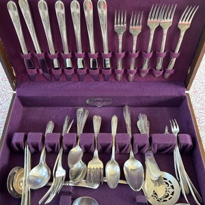 May include: A wooden box with a purple velvet interior containing a set of silver plated flatware. The flatware includes knives, forks, spoons, and a serving spoon. The box has a label that reads "Solidity Plate Guaranteed by Good Housekeeping".