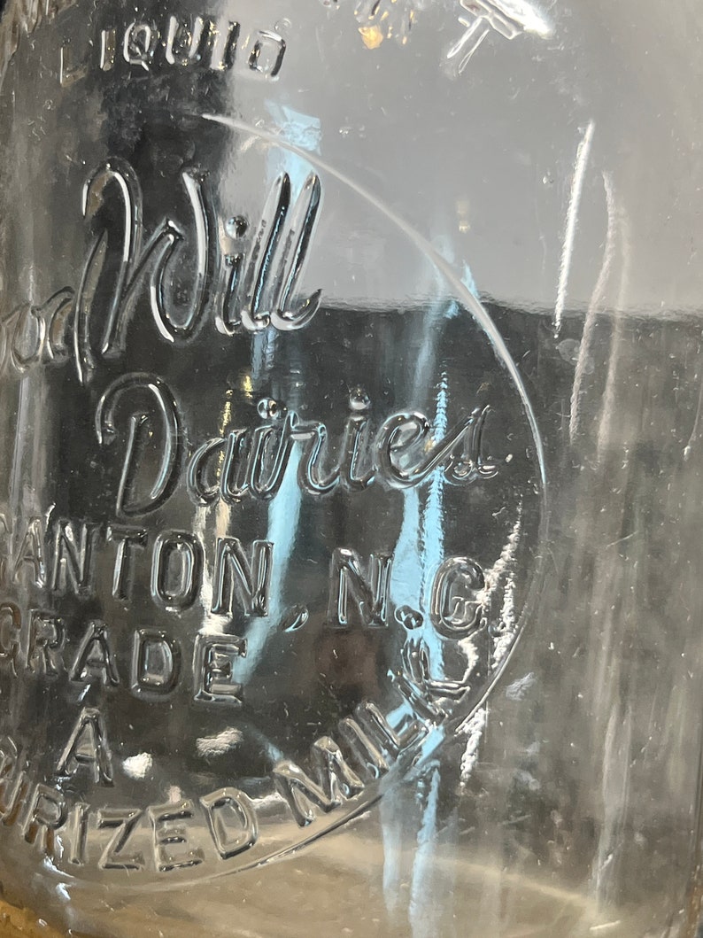 May include: A vintage glass milk bottle with the text "Good Will Dairies, Canton, N.C. Grade A" embossed on the side.